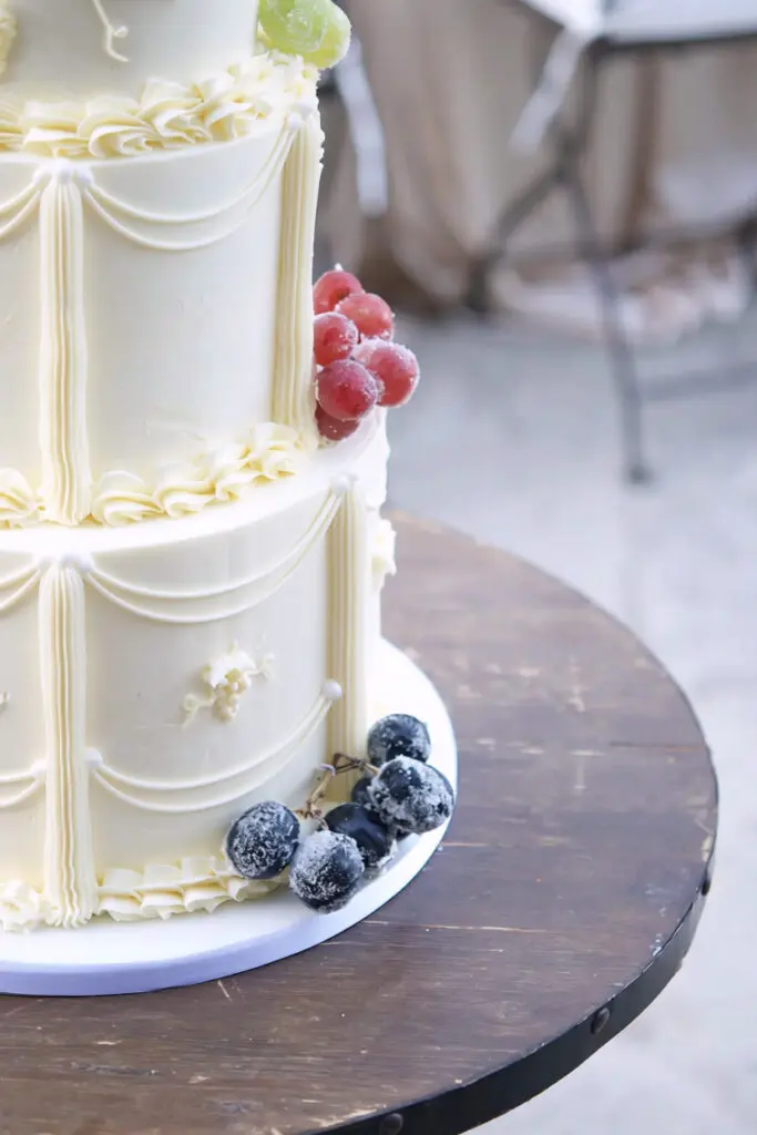 Red and black sugared grapes on the base tier of a piped wedding cake