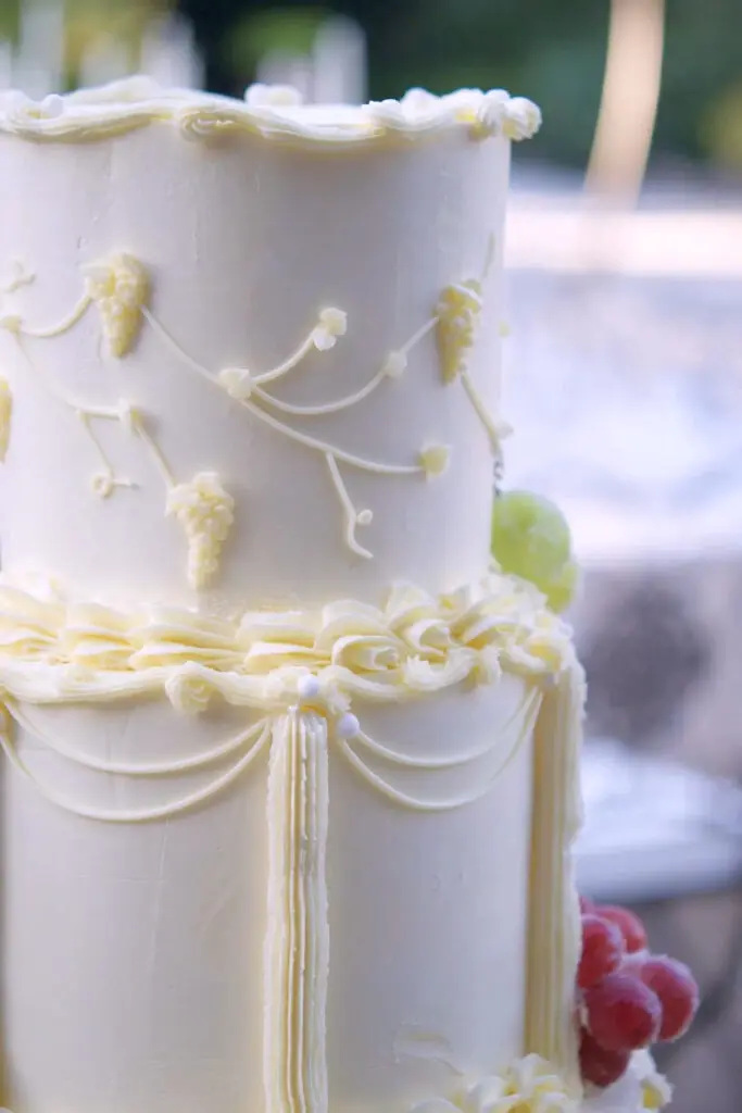 Close-up of hand-piped grape bunches and vines on a buttercream wedding cake