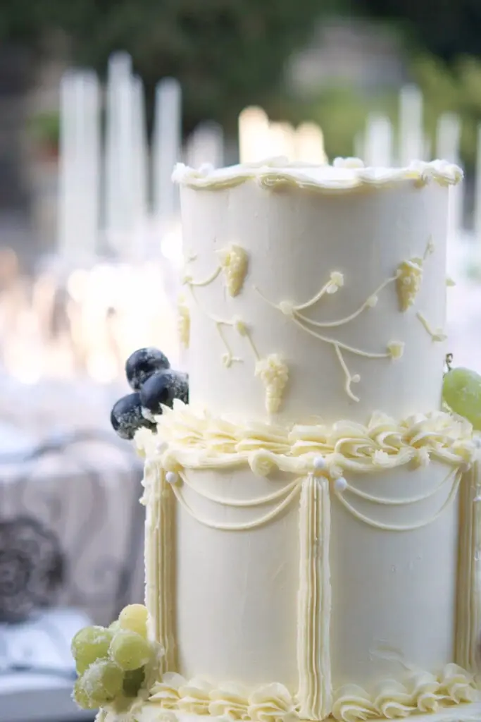 Top tiers of a vintage wedding cake with hand-piped grapes, vines and garlands
