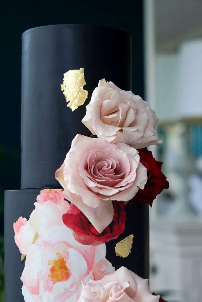 Detail of gold leaf and watercolour roses on a black fondant wedding cake