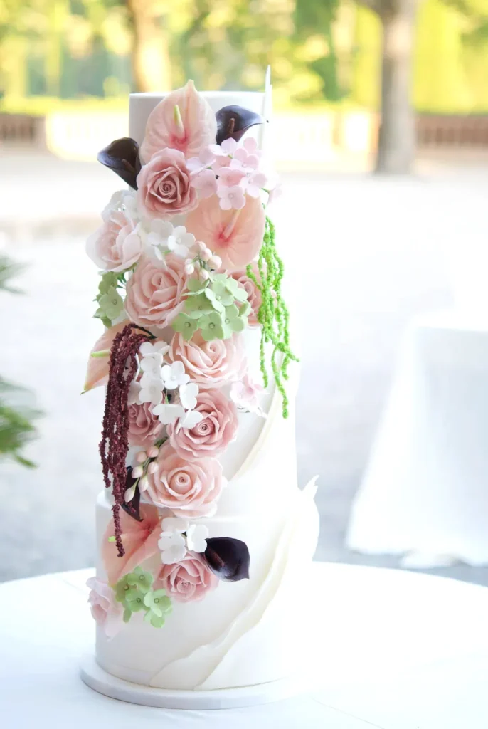Four-tier wedding cake with draped fondant and a cascading arrangement of sugar flowers