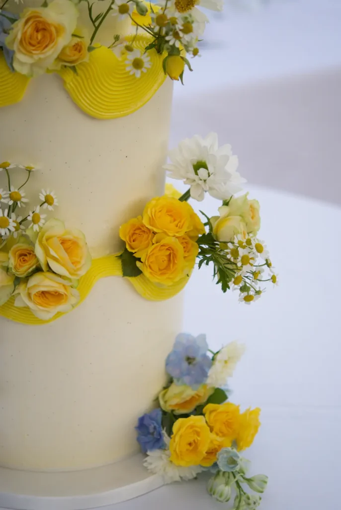 Close-up of yellow roses and daisies on a white wedding cake